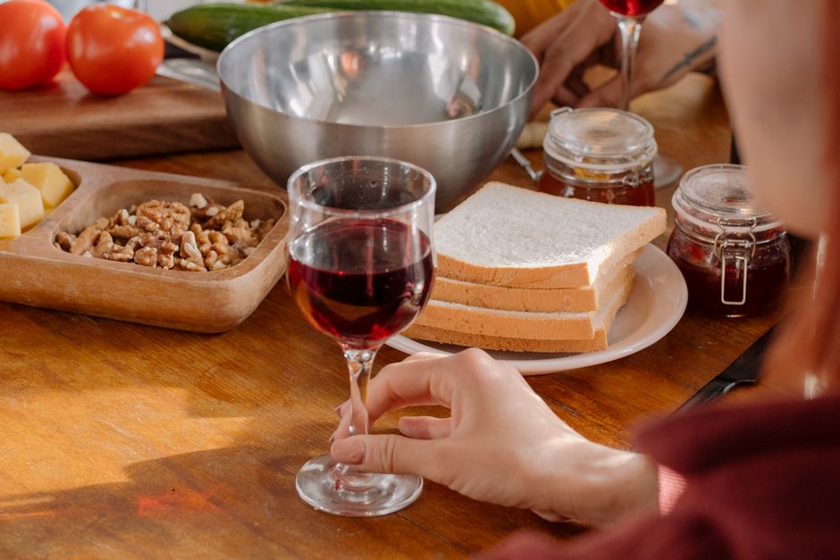 A person enjoying wine while preparing a meal with fresh ingredients and bread.
