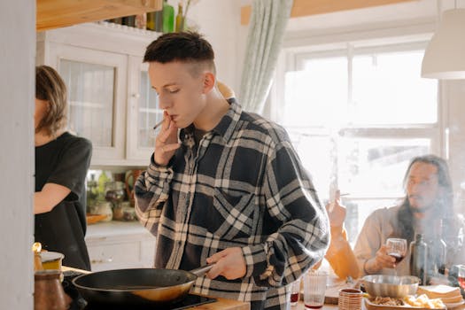 Three young adults enjoy cooking and smoking together in a bright, cozy kitchen setting.