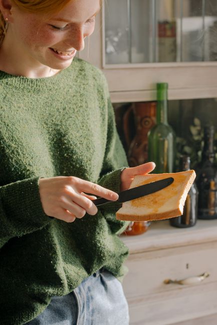 Smiling young woman spreading jam on toast in a cozy kitchen.
