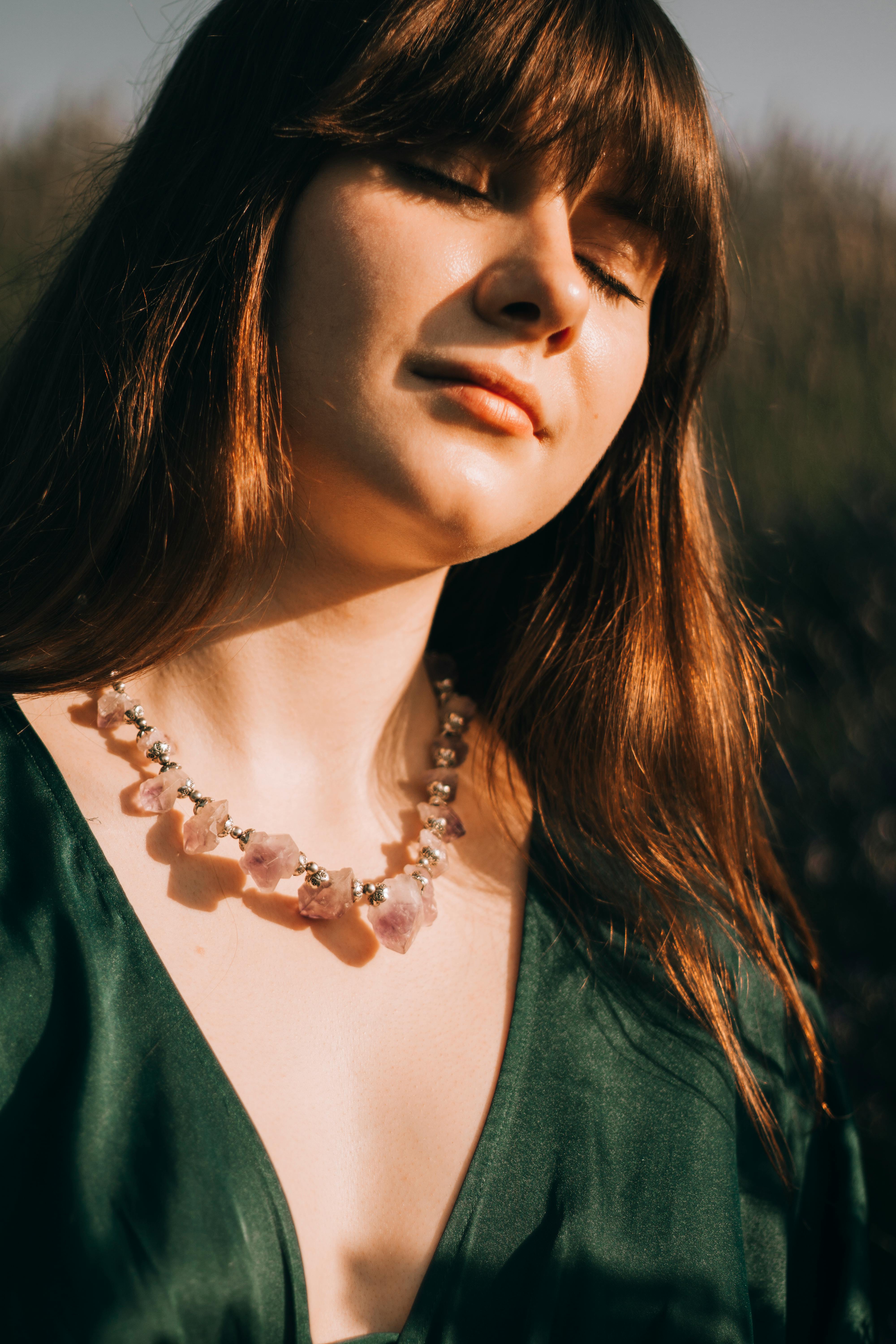 Young charming chubby female with eyes closed and plump lips wearing beads in green provocative blouse