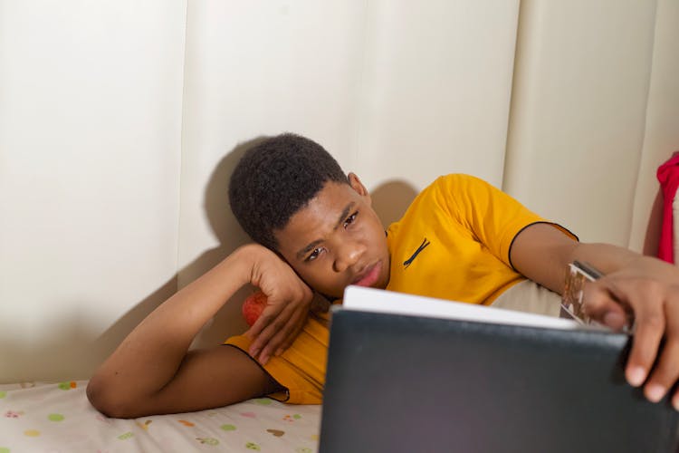 Photo Of A Boy In A Yellow Shirt Reading On A Black Book