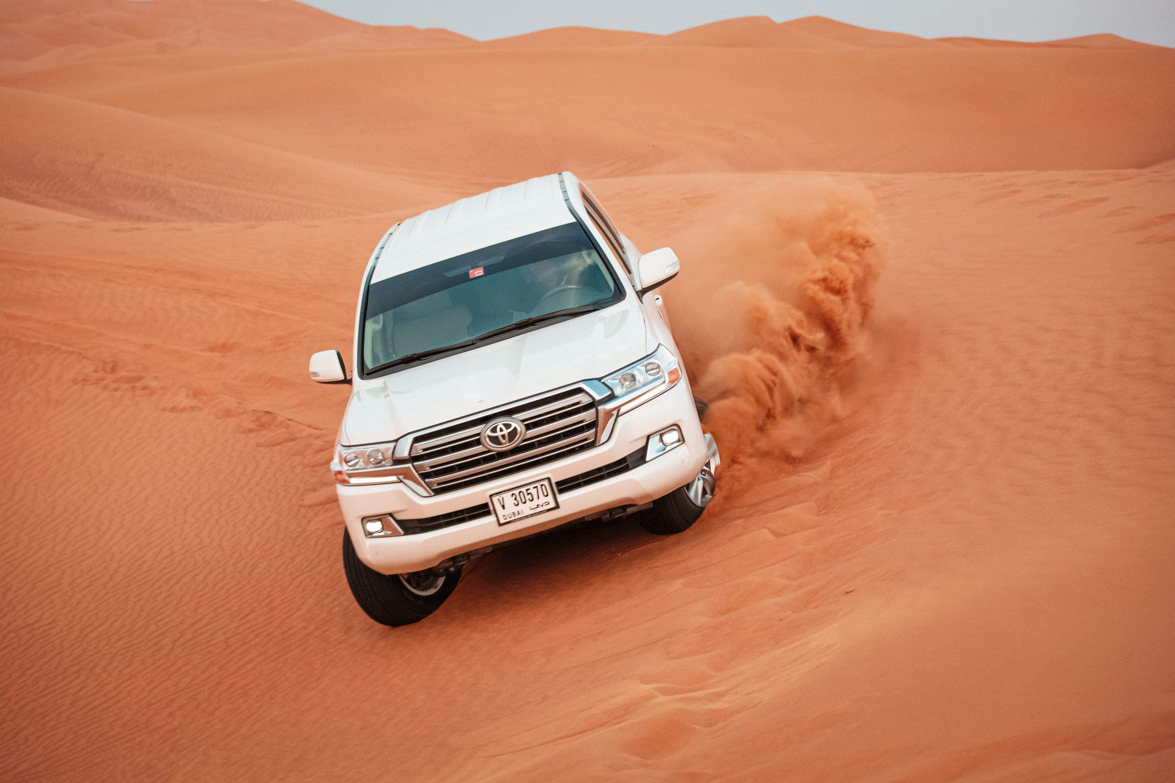 White Toyota Land Cruiser kicking up sand while driving across desert dunes — soft-surface off-road sand driving