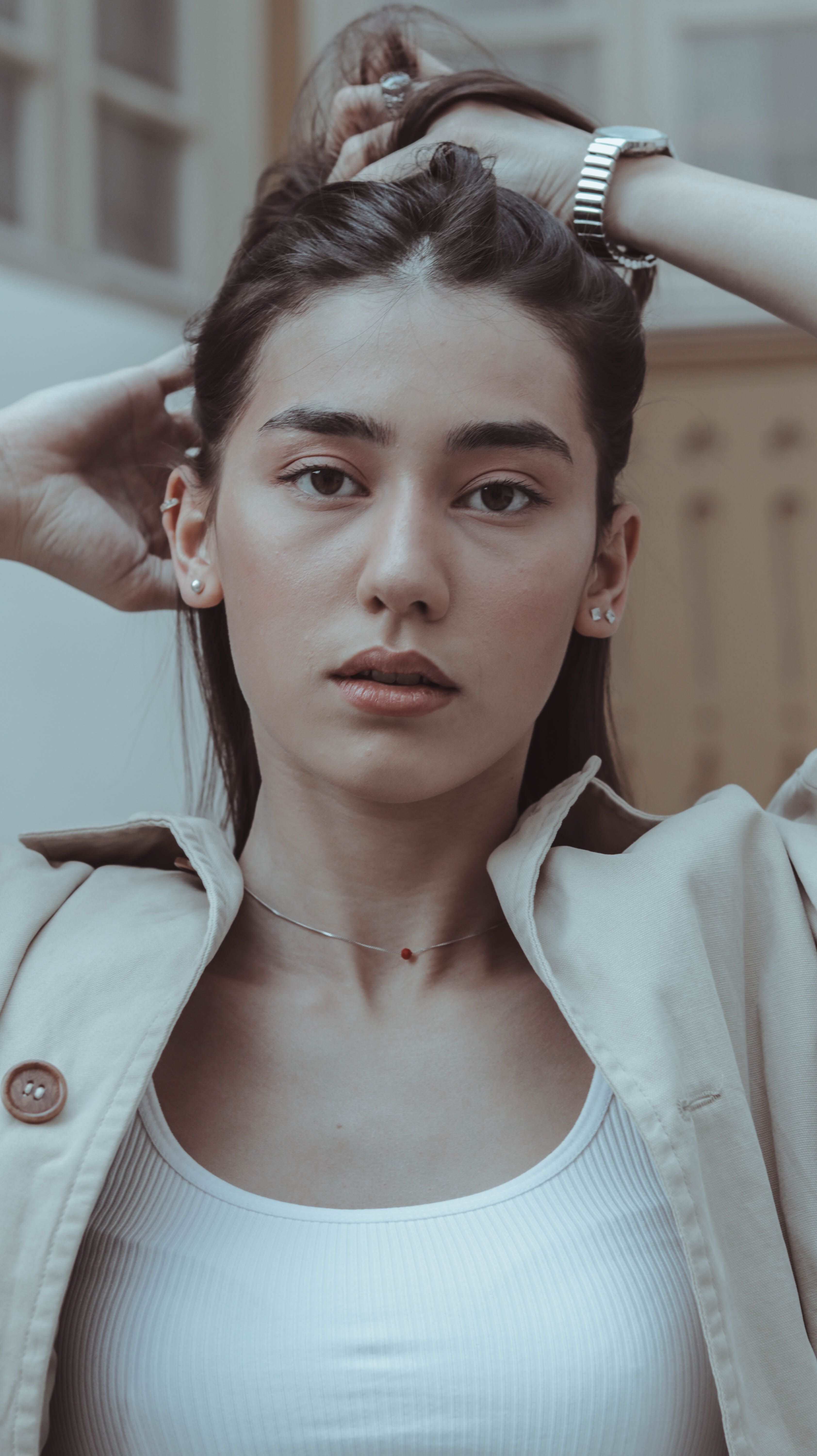 Confident young female with hands on head touching hair while thoughtfully looking at camera