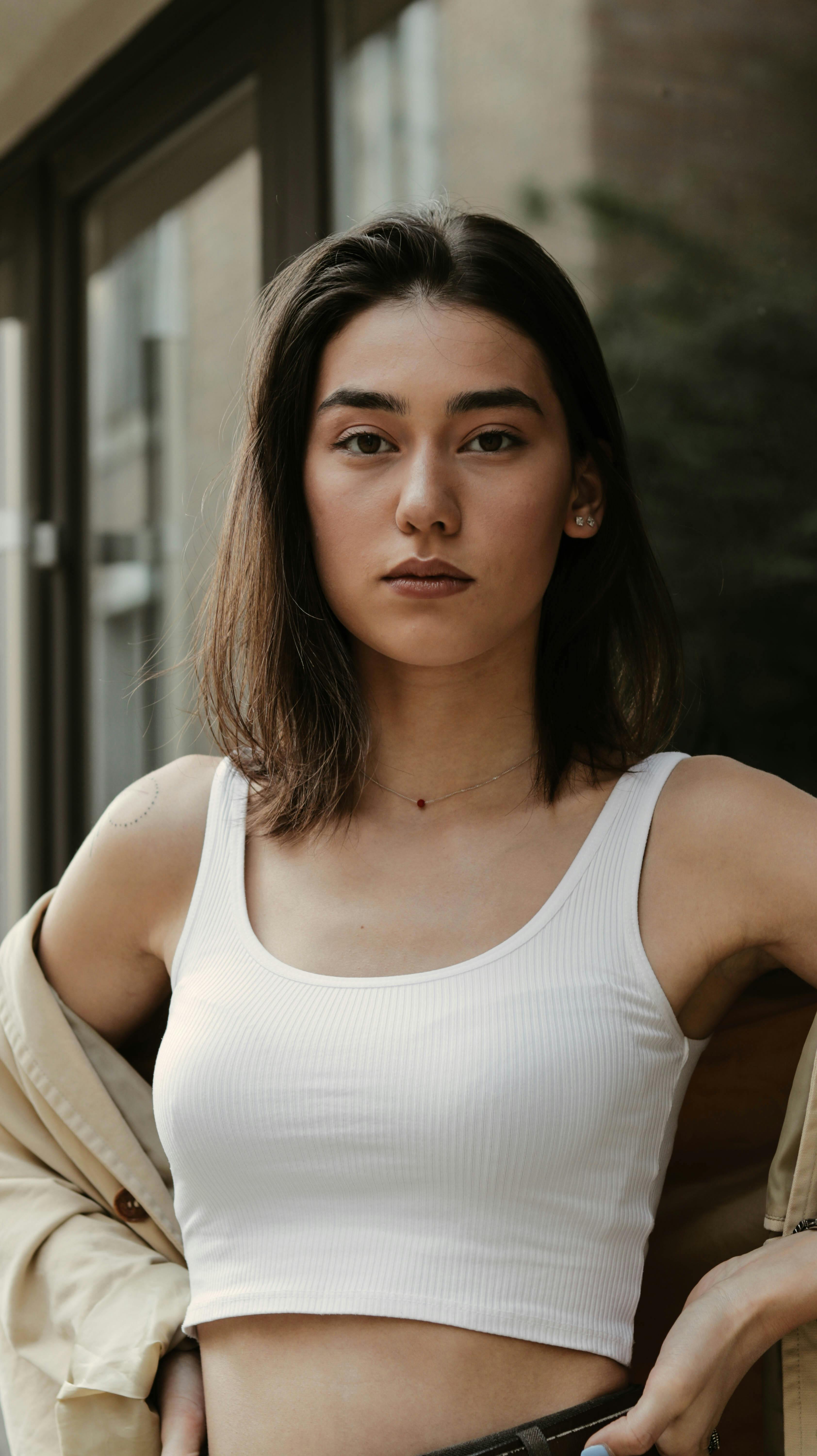 Confident young female wearing casual clothes standing with hands on waist and thinking while looking at camera