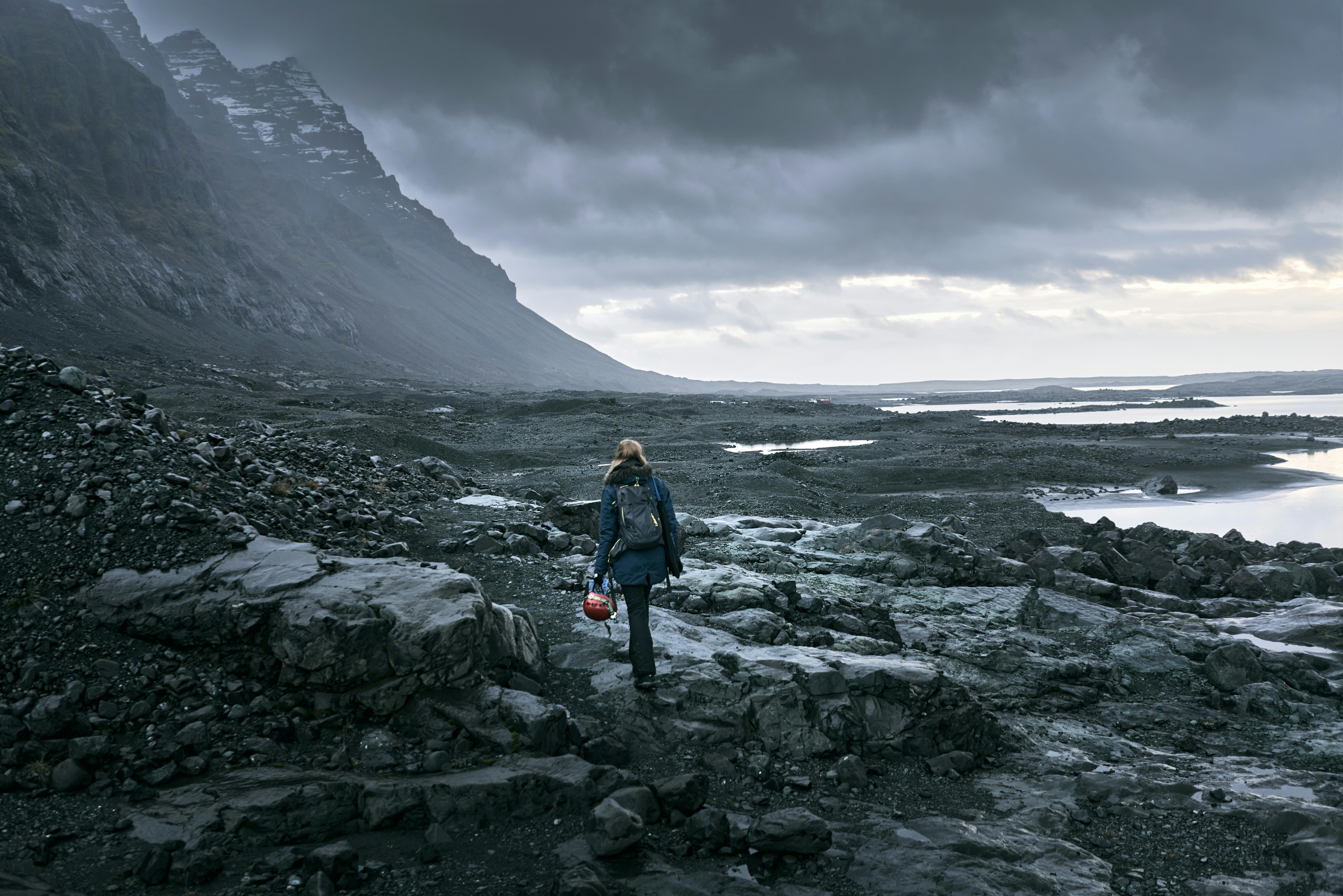 徒步旅行者背着背包，在阴沉的天空下穿越冰岛的岩石景观