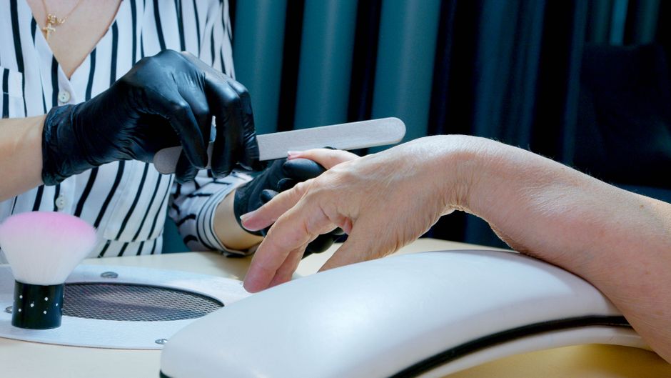 Close-up of a manicurist filing nails, providing professional salon service with gloves.