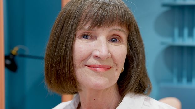 一张友好的特写镜头捕捉到了一位面带微笑、棕色短发的老年女性在室内的肖像