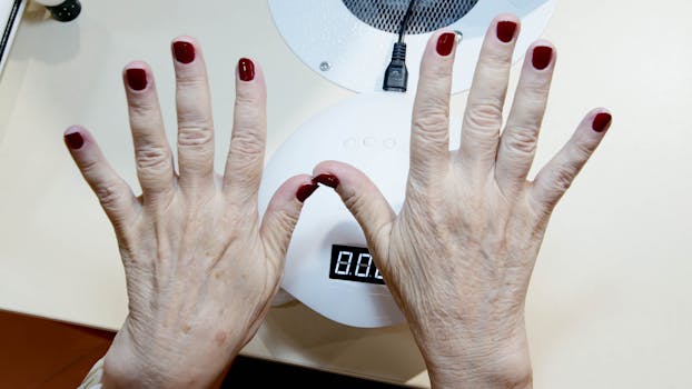Close-up of senior woman's hands with red nails under drying lamp in salon.