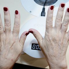 Two hands with red nails held above a white dome nail lamp with a digital timer