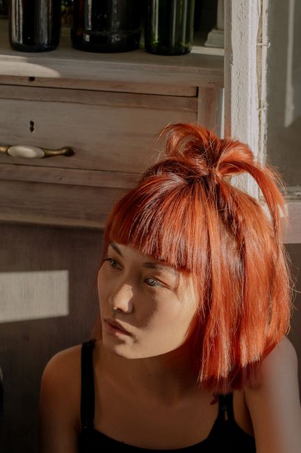 Close-up portrait of a woman with red hair, sitting in sunlight indoors, looking contemplative.