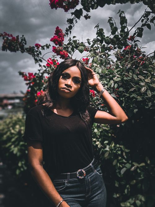 Free Woman in casual attire standing among vibrant red blossoms on an overcast day. Stock Photo