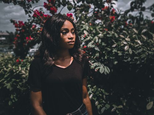 Free Beautiful woman in black t-shirt standing among red flowers outdoors in natural light. Stock Photo
