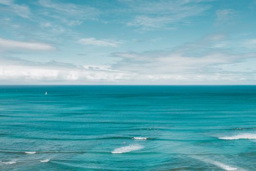 Serene view of a vast ocean horizon with gentle waves and a distant sailboat under a clear sky.