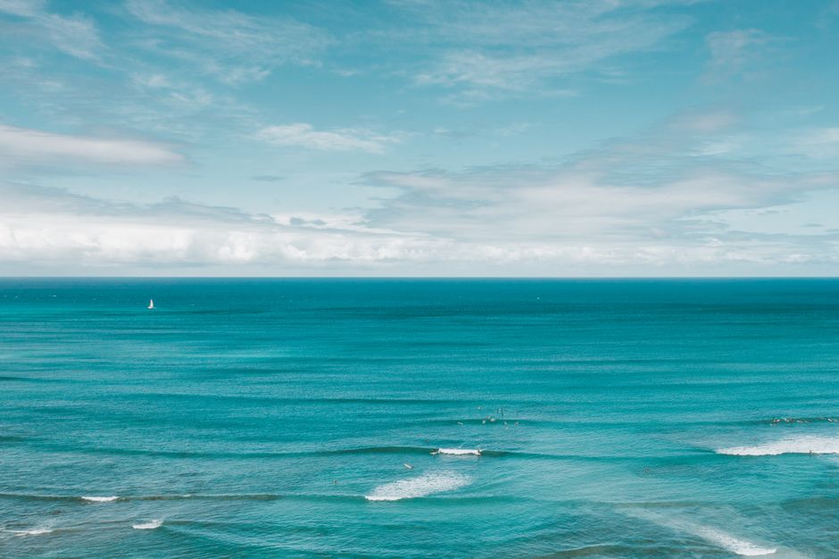 Serene view of a vast ocean horizon with gentle waves and a distant sailboat under a clear sky.