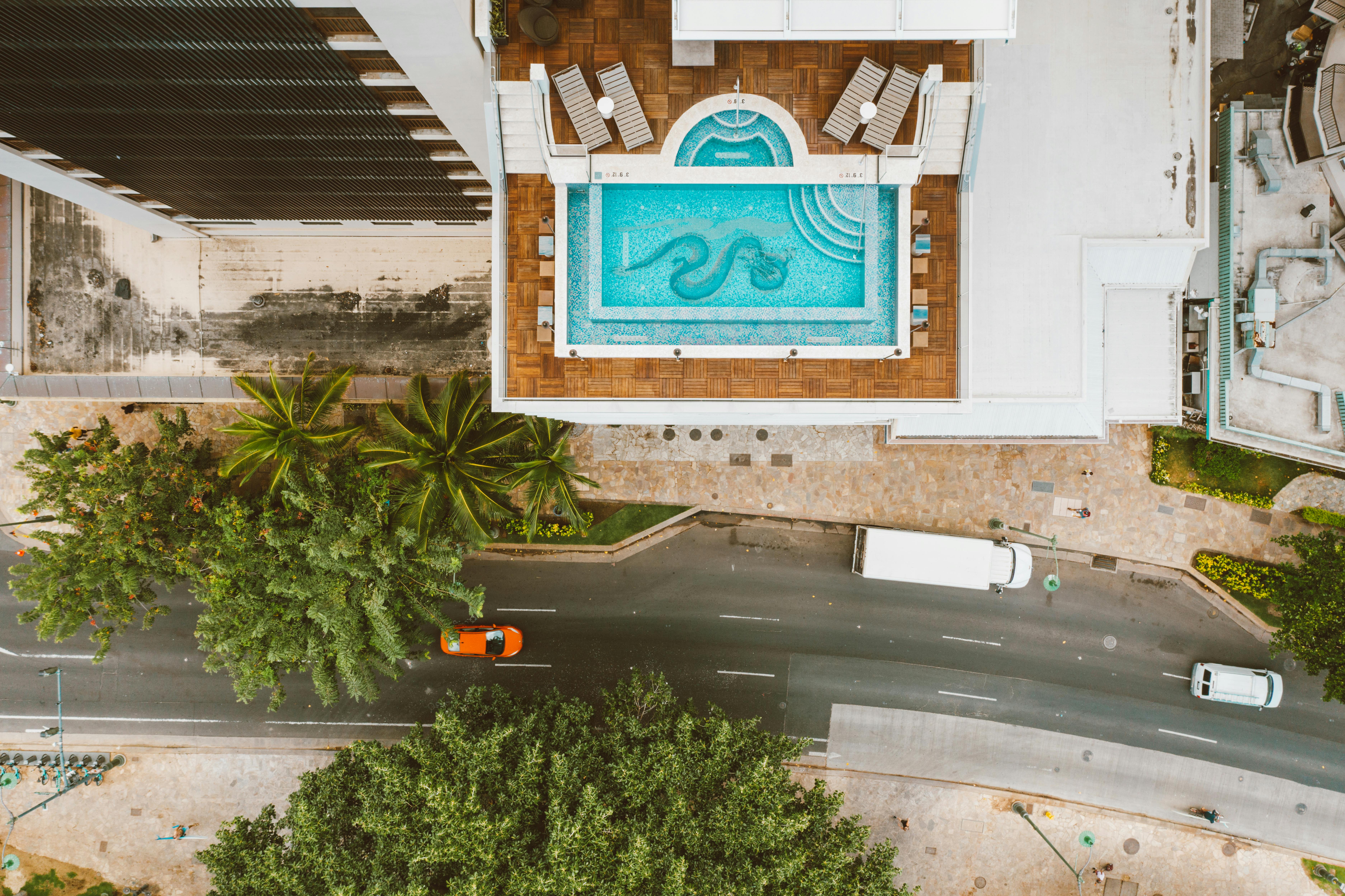 航拍照片中，屋顶游泳池和城市街道周围环绕着绿化植物与车辆