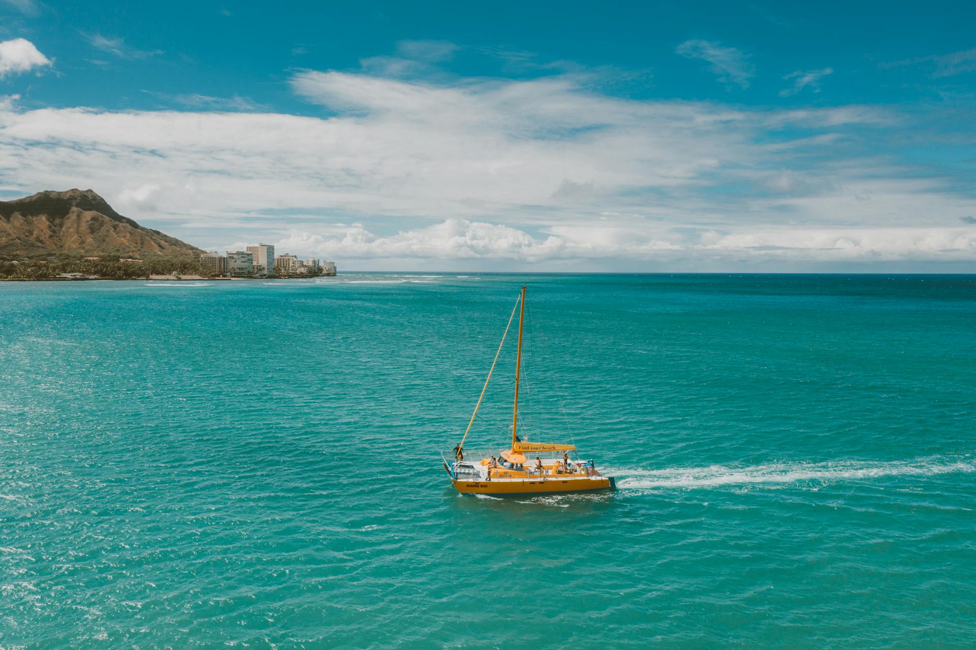 A vibrant sailboat cruises on the stunning turquoise waters near Waikiki with a scenic view of the coastline.