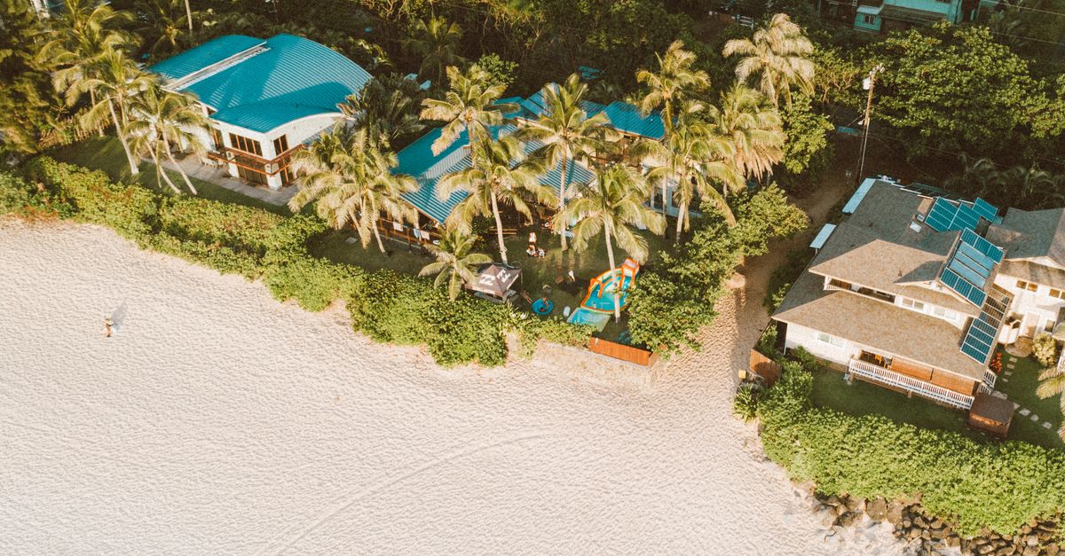 Aerial shot of a tropical resort with palm trees and sandy beach at sunset.