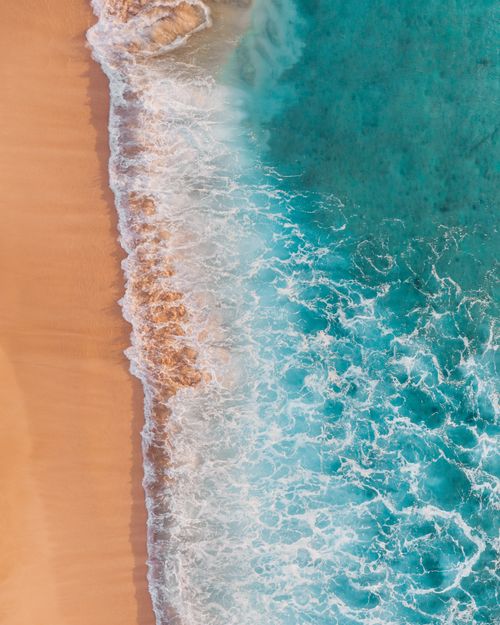 Free A stunning top-down view of turquoise waves crashing on a sandy beach, captured from above. Stock Photo