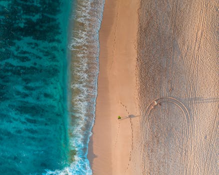A stunning aerial view of a tranquil beach with turquoise waves and footprints in the sand.