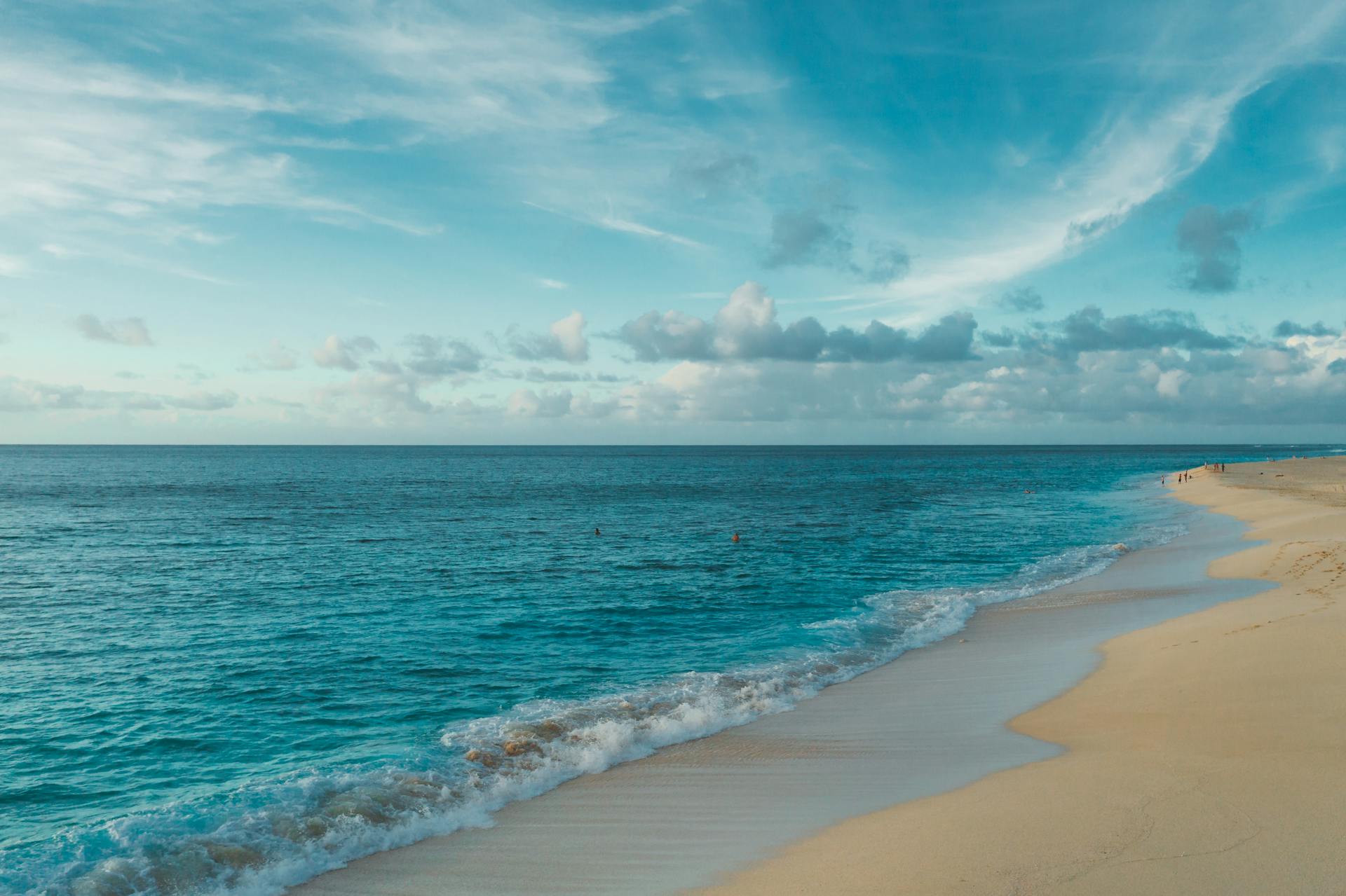 Serene beach landscape with clear blue ocean and clouds under a bright sky.