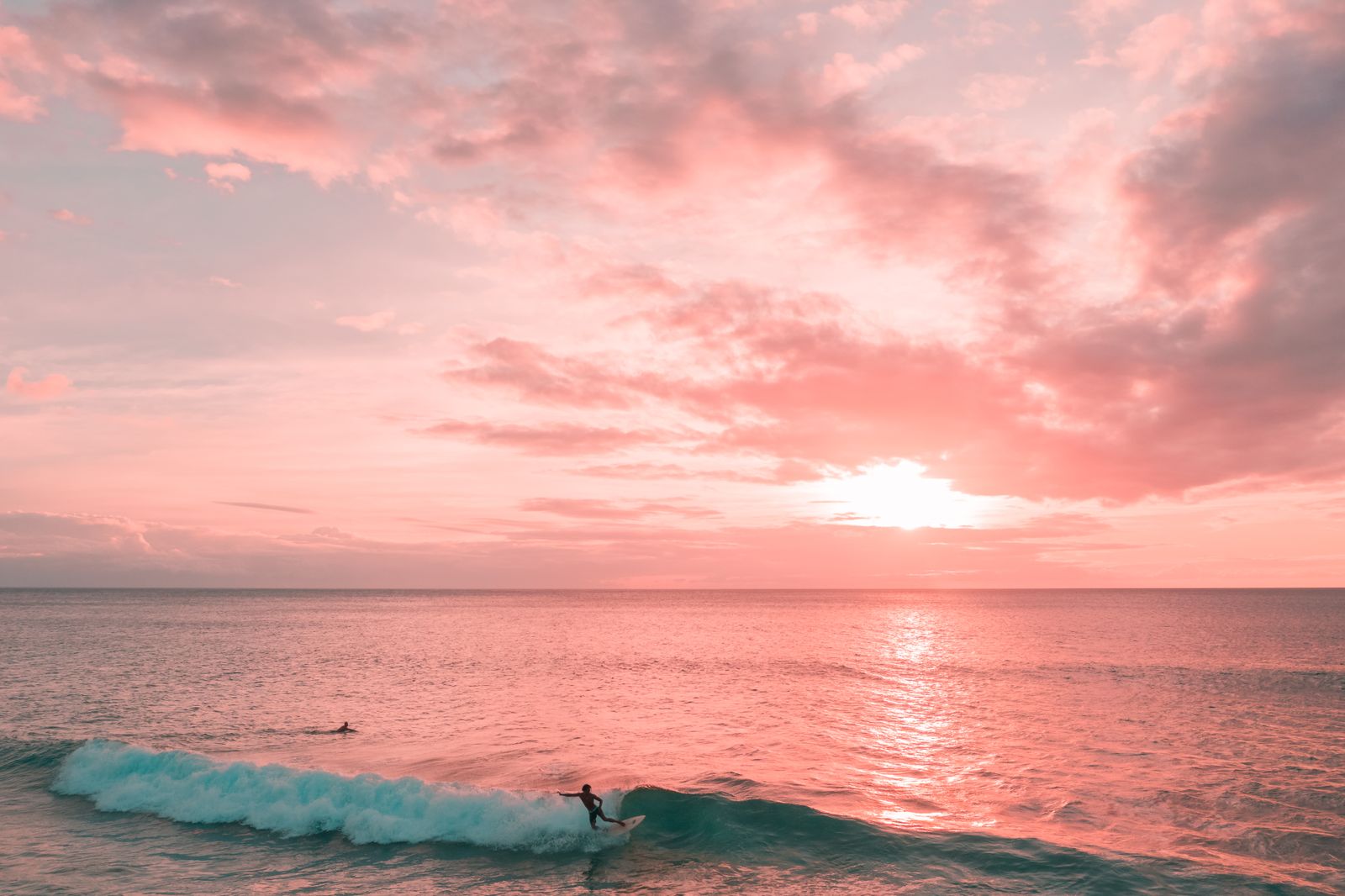 A surfer beneath a pink evening sky