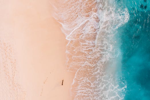 Stunning aerial shot of a sandy beach meeting turquoise ocean waves, perfect for travel and nature themes.