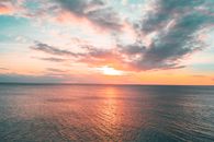 这幅宁静的沿海画面令人惊叹：海洋日落与天空中充满活力的珊瑚色和茶色调交相辉映