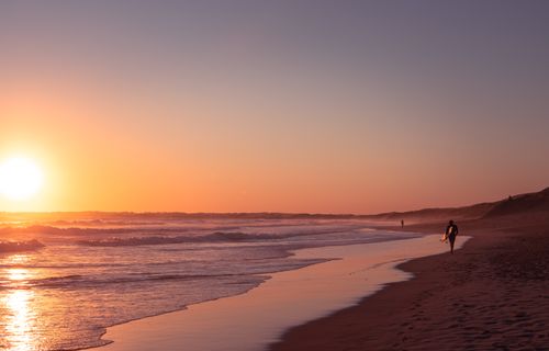 Free A lone surfer walks along a serene Australian beach at sunset, capturing a peaceful moment by the sea. Stock Photo