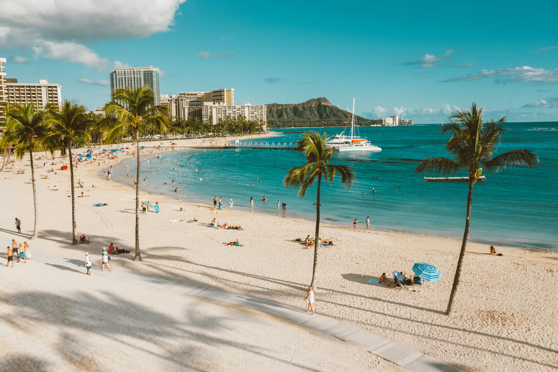 Sunny day at Waikiki Beach with a view of Diamond Head and people enjoying the ocean.