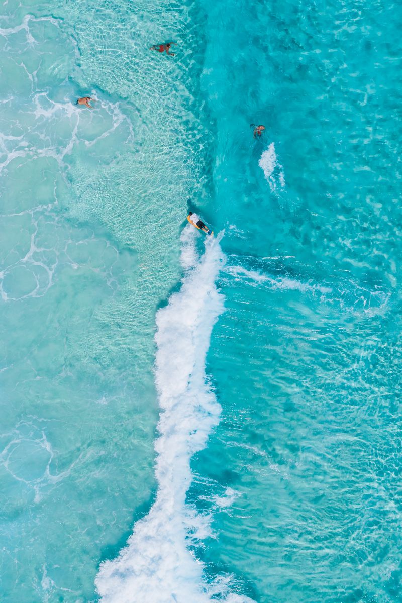 Dynamic aerial shot of surfers riding vibrant turquoise and white waves in the ocean.