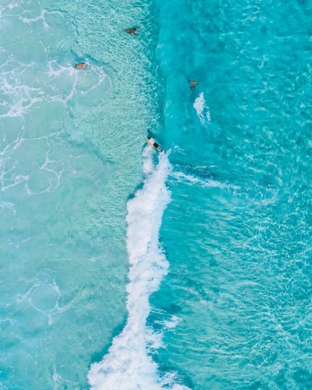 Aerial view of surfers paddling into turquoise water — photo by Jess Loiterton on Pexels