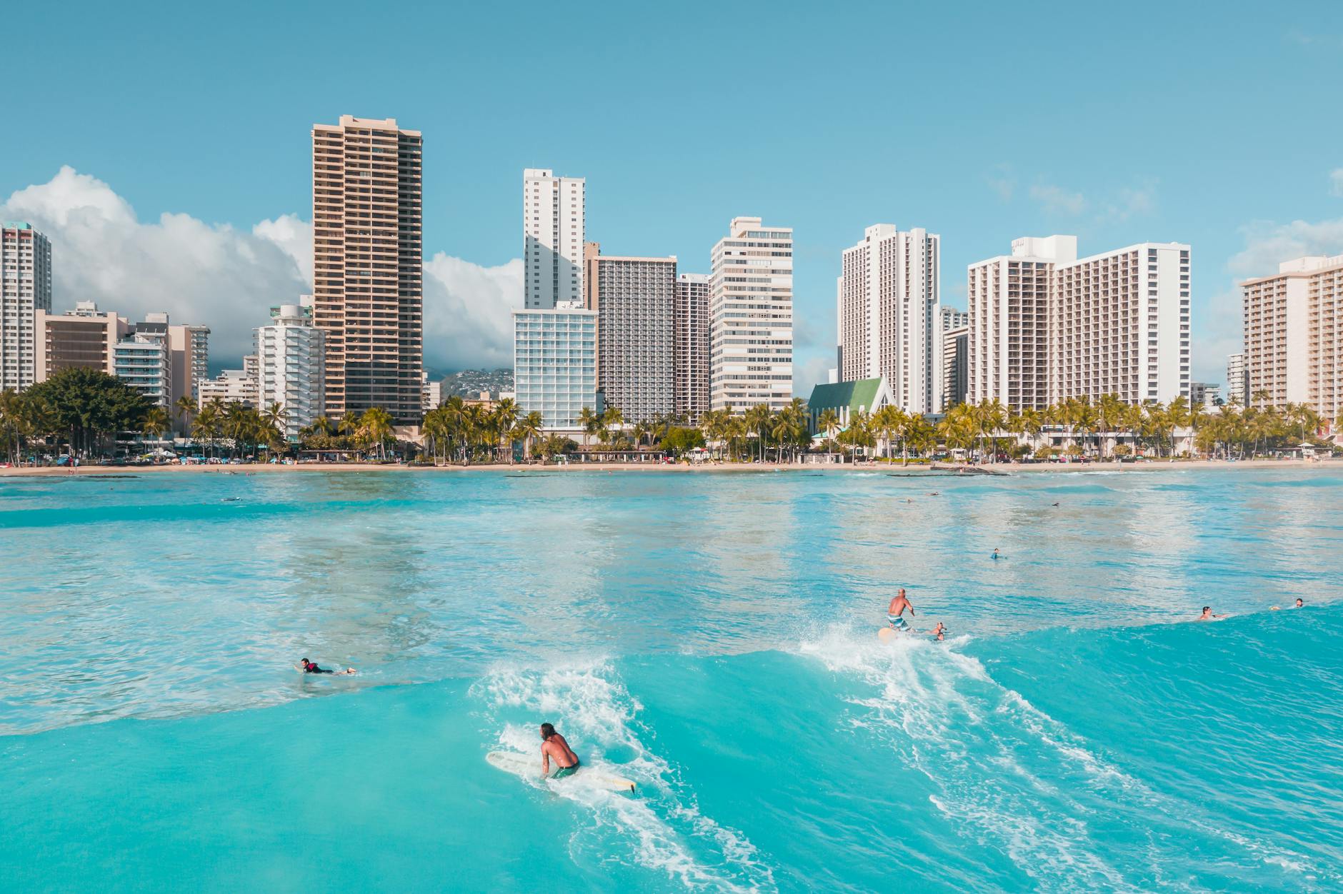 Dynamic surfers ride waves against a backdrop of a vibrant coastal city skyline, showcasing leisure and recreation.