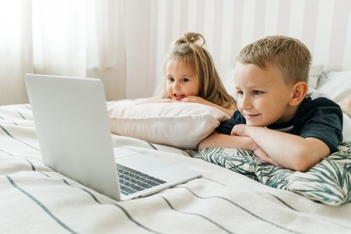 Free Two children watching a laptop while lounging on a comfortable bed indoors. Stock Photo