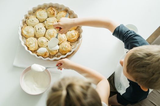 Overhead shot of children spreading cream on homemade cinnamon rolls, enjoying a family breakfast.