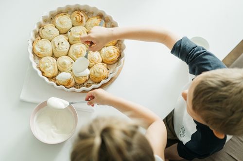 Free Overhead shot of children spreading cream on homemade cinnamon rolls, enjoying a family breakfast. Stock Photo