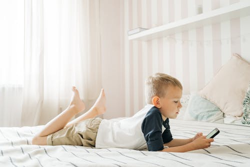 Free A Boy Using a Smartphone on the Bed Stock Photo