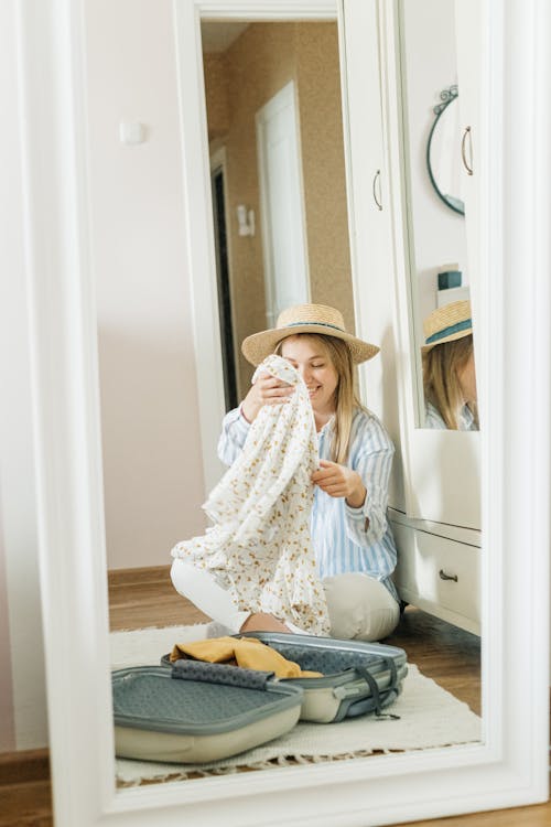 Free A Woman Wearing a Sun Hat Packing Clothes in a Suitcase Stock Photo