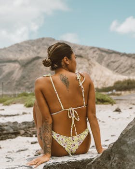 夏天，一位穿着比基尼的纹身女人在岩石海滩上休息，享受放松和自然