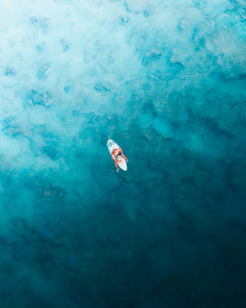 Person Sitting on the Surfboard on the Sea