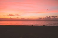 宁静的海滩日落，以充满活力的色调和剪影人物映衬着海洋地平线
