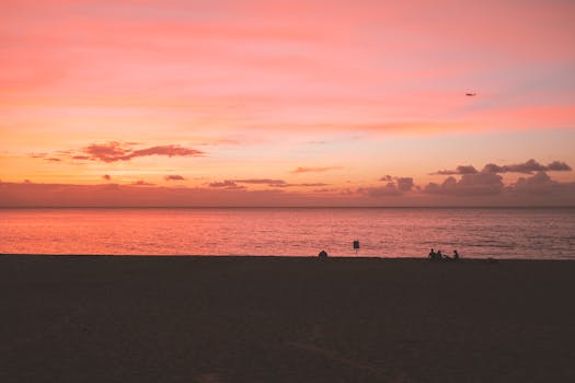 宁静的海滩日落，以充满活力的色调和剪影人物映衬着海洋地平线