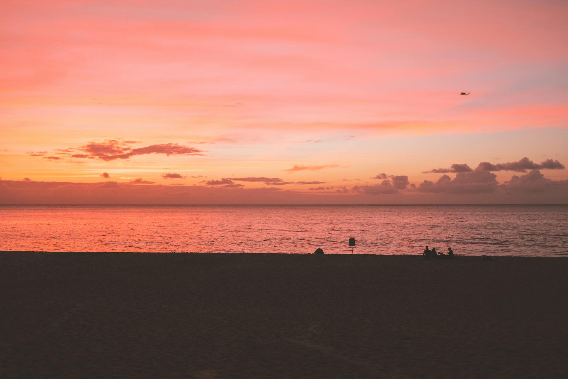A tranquil beach sunset with vibrant hues and silhouetted figures against the ocean horizon.
