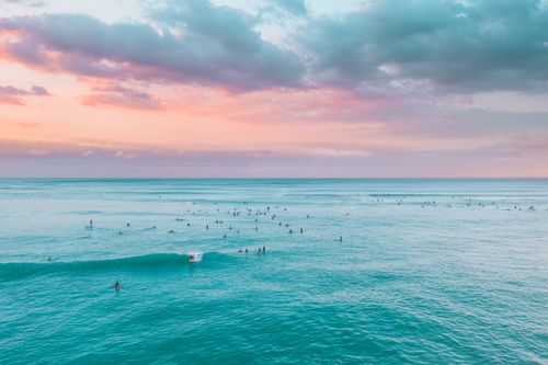 Free A breathtaking view of surfers enjoying the ocean during a vibrant sunset with turquoise waters and pastel skies. Stock Photo