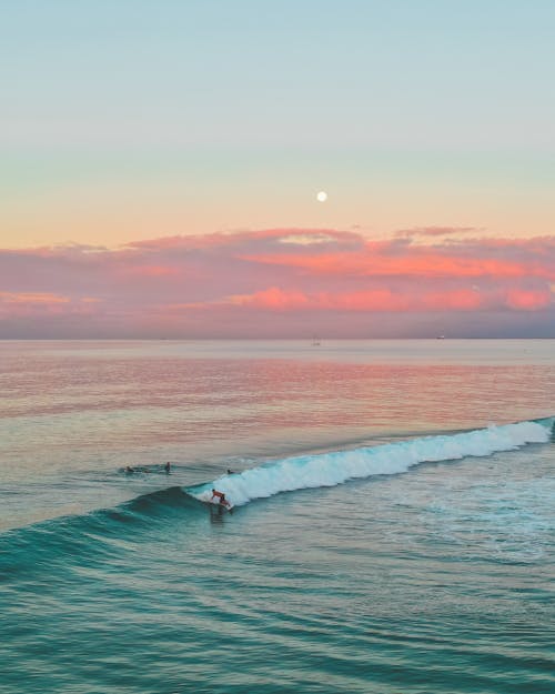 Person Surfing on Ocean Waves Under Twilight Sky 
