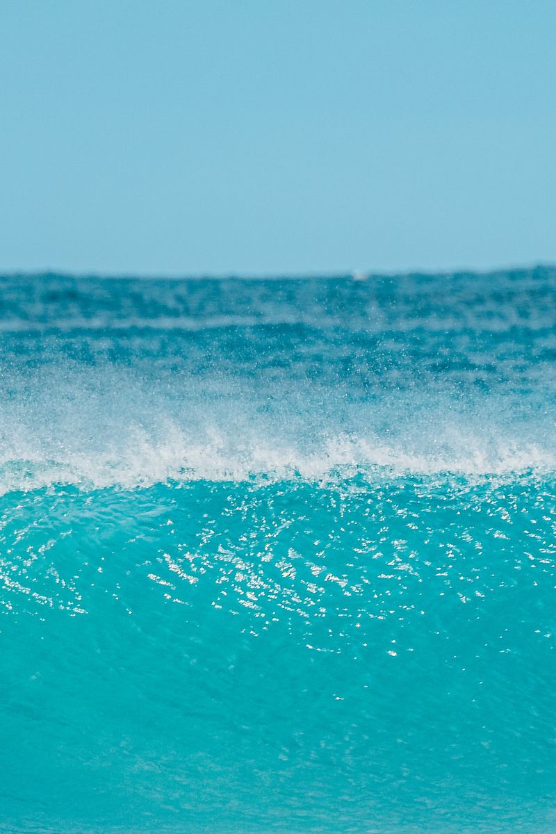 Vibrant ocean wave crashing under a clear blue sky, capturing the serenity of nature.