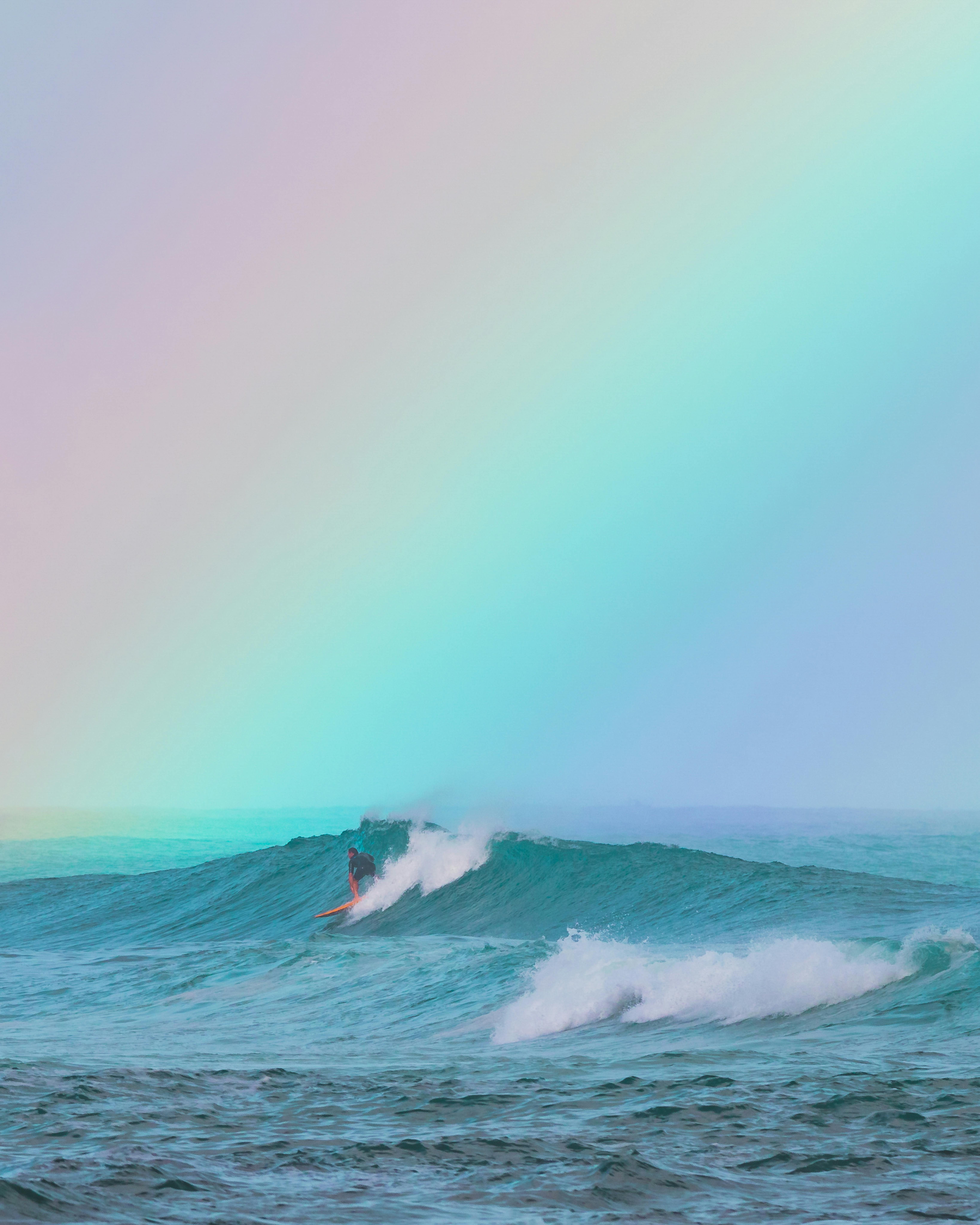 一名冲浪者在海洋上五彩缤纷的彩虹下捕捉海浪，享受激动人心的户外冒险