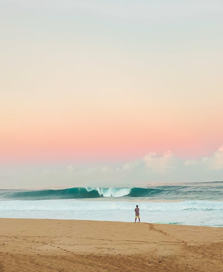 Person Standing And Looking At The Waves On The Sea At Sunset 