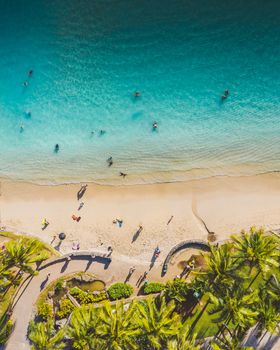 Aerial view of a vibrant tropical beach with turquoise water, palm trees, and people enjoying summer.