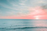日落时分，海面宁静，天空泛着粉红，水中游泳者的轮廓清晰可见