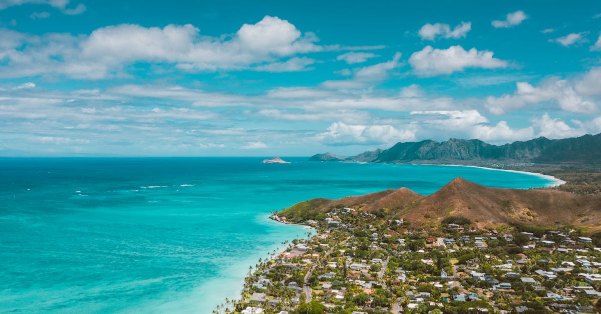Photo by Jess Loiterton A scenic aerial shot of a tropical town by the ocean with turquoise waters and mountain ranges.